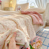 A hand is holding a pink floral quilt blanket with a soft washed finish on a bed.