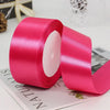 A roll of bright pink satin ribbon used for gift wrapping and crafts, lying on a white surface.