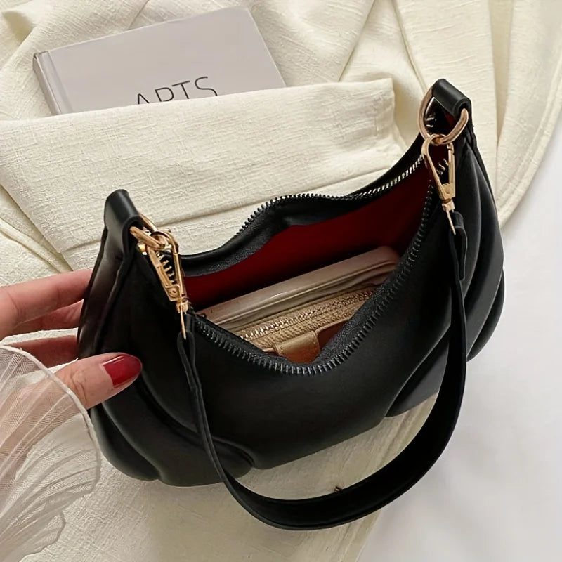 A black women's textured crossbody bag with a gold-toned chain detail is shown against a cream fabric background.