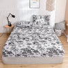 A fitted bed sheet with a marbled print featuring black and white tree motifs is displayed on a bed.