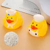 A yellow rubber duck bath toy with an orange beak and white details is shown next to a pile of small white beads.