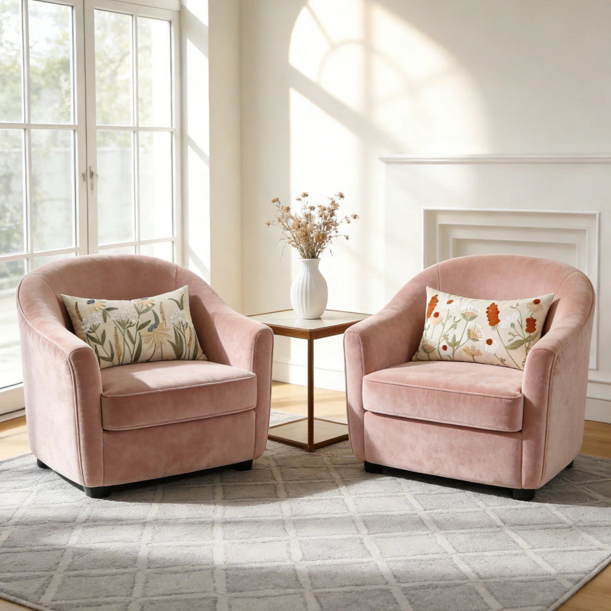 Two pink upholstered armchairs with floral embroidered pillows sit by a bright window in a light-filled room.