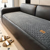 A dark gray quilted plush sofa cover with a black leather frame and non-slip backing is shown on a floor.