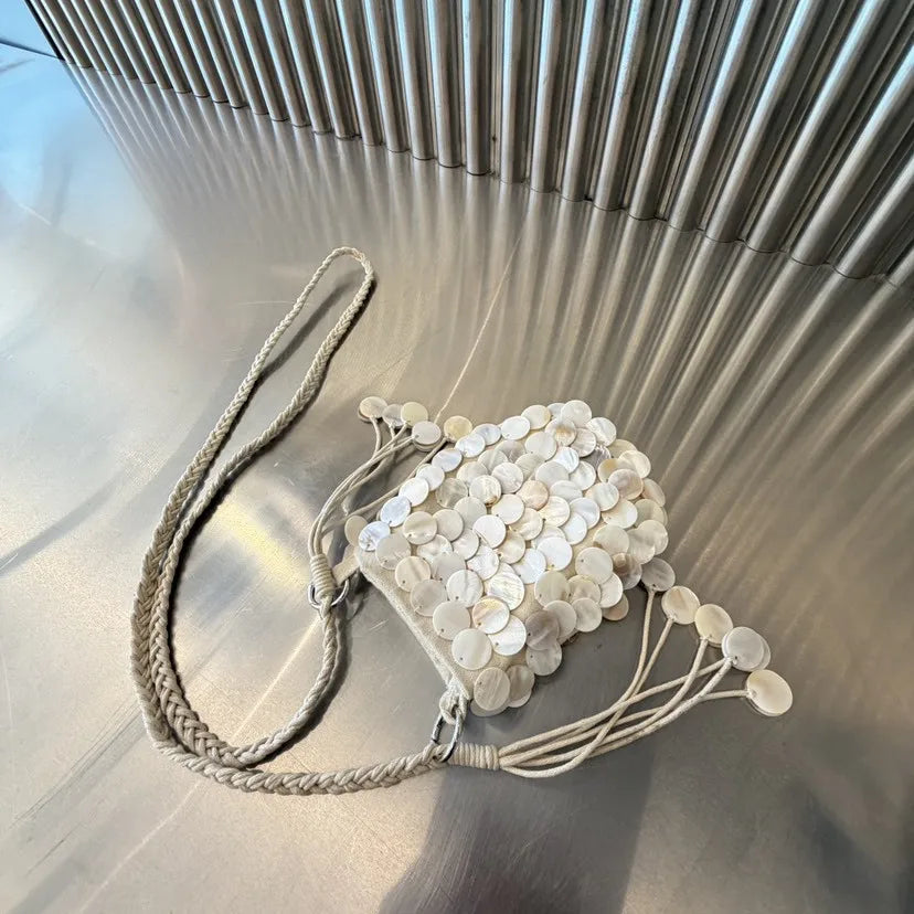 A light beige sequin accent chain shoulder bag with a delicate leather strap resting on a reflective surface.