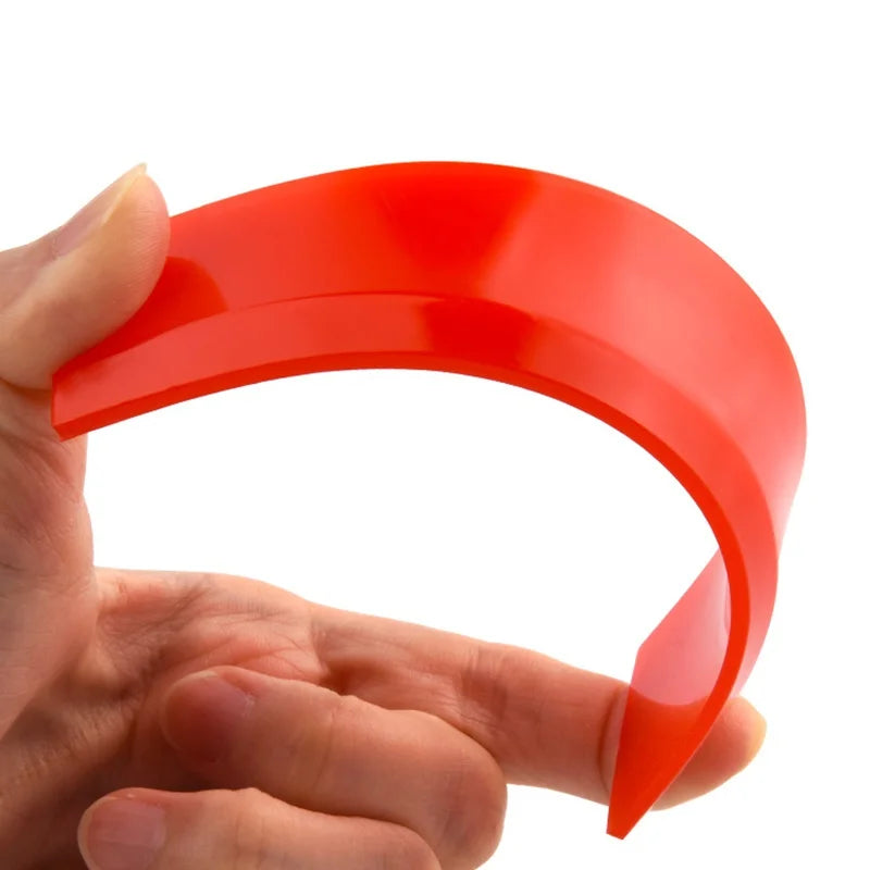 A hand holds a bright red silicone grout and sealant scraper tool, showing its curved shape.
