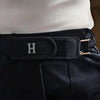 A close-up of a black hook belt with a silver initial H buckle on a person's waist.