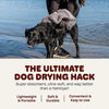 A black dog is standing in shallow water with a gray towel draped over its body.