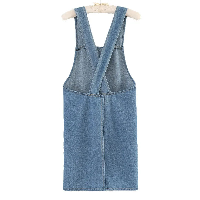 A denim cross-back apron with a V-neck and front pockets is displayed on a hanger.