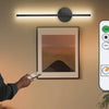 A man is adjusting a wall-mounted LED light fixture with a remote control, demonstrating the dimmable lighting functions.