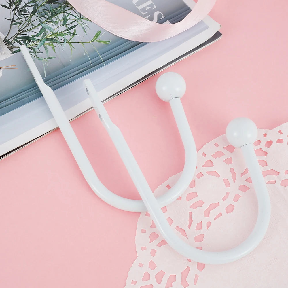 A set of two white U-shaped tieback hooks with long handles resting on a pink fabric surface.