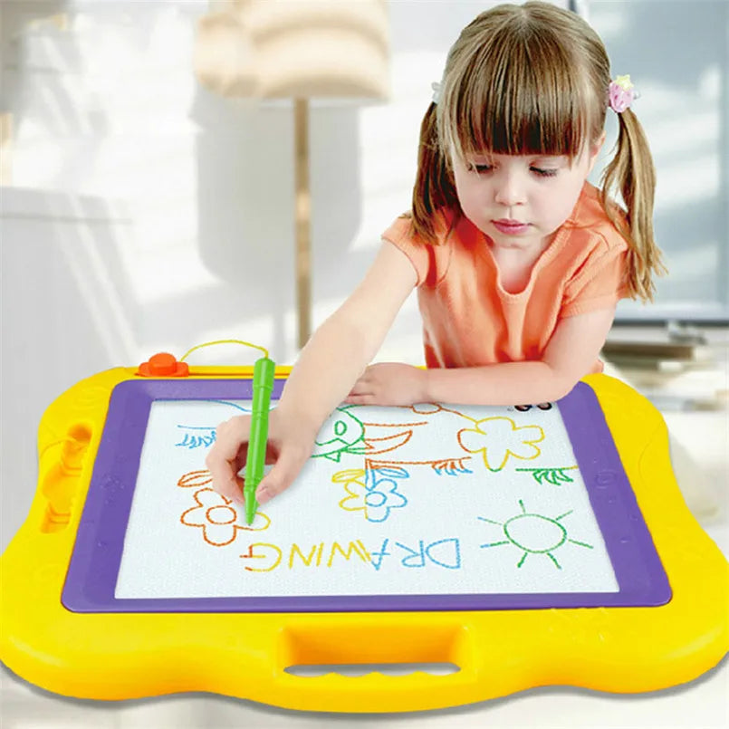 A young girl is drawing on a large yellow magnetic board with green markers.