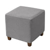 A square ottoman slipcover in a gray woven fabric with an elastic edge.