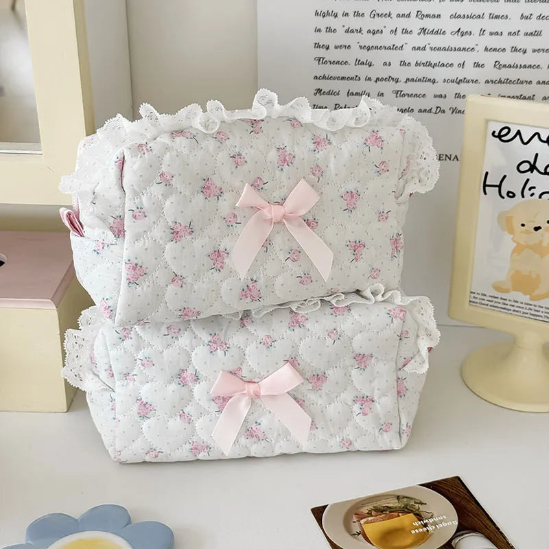 A white cosmetic pouch with a vintage rose print and pink satin ribbon bow, featuring delicate lace trim.