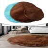 A round, shaggy brown faux fur rug is shown in an overhead view against a modern interior setting.