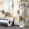 Roll of gold foil marble peel-and-stick wallpaper displayed next to a marbled wall texture.