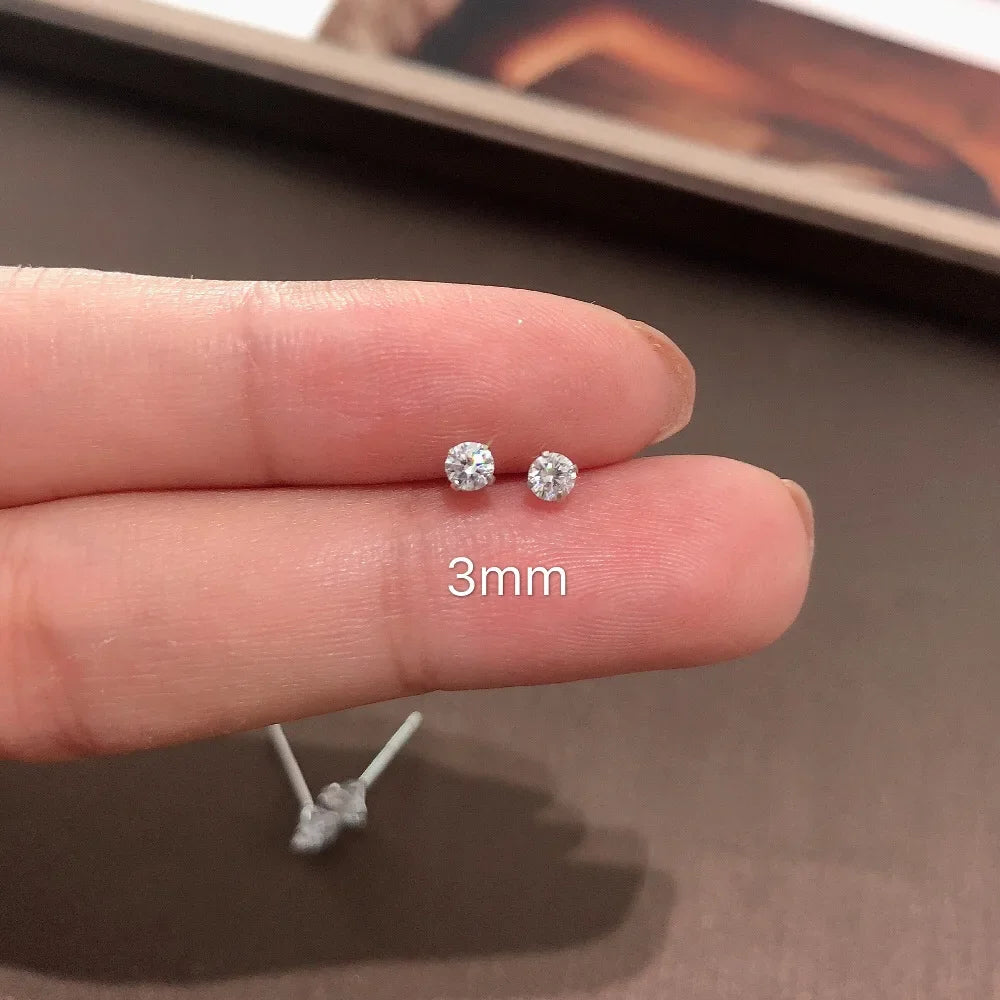 Une main tient une paire de minuscules clous d'oreilles en cristal clair sur un doigt, avec un marqueur d'échelle de 3 mm à p