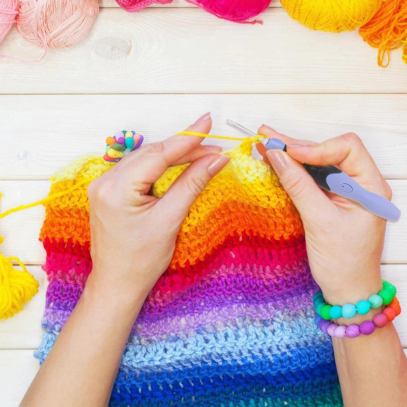 Hands knitting a colorful rainbow scarf using a crochet hook set with nine interchangeable heads