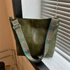 A dark olive green vintage bohemian shoulder bag with golden embroidery hanging in front of a window blind.