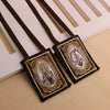 A brown leather scapular necklace with an ornate pendant featuring a religious figure on a dark fabric background.
