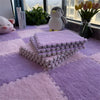Purple and pink plush interlocking floor tiles stacked on a purple rug with a penguin toy and flowers in the background