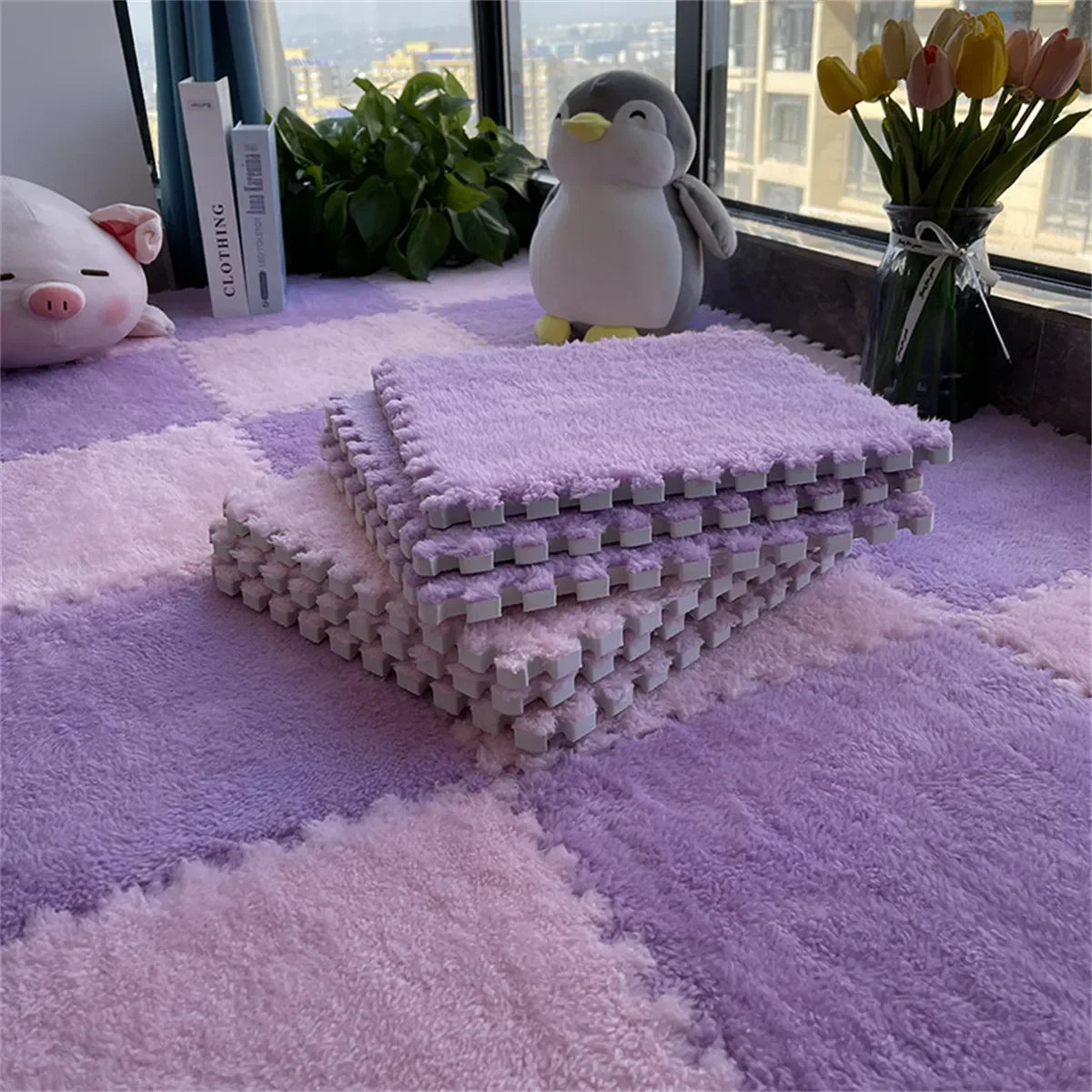 Purple and pink plush interlocking floor tiles stacked on a purple rug with a penguin toy and flowers in the background