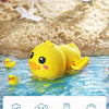 A yellow wind-up bath toy duck floating in blue water near a sandy beach background.
