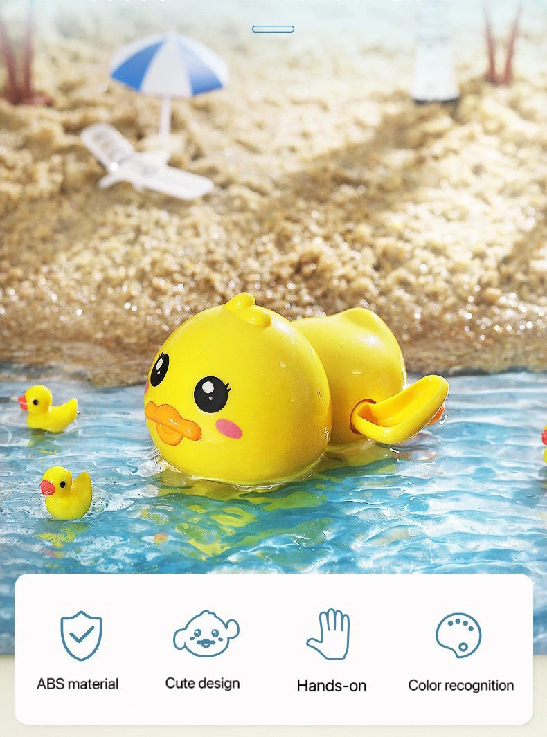 A yellow wind-up bath toy duck floating in blue water near a sandy beach background.