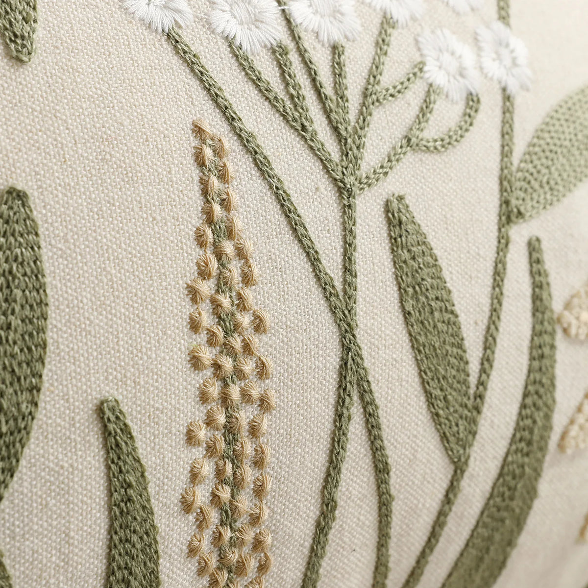 Close-up of a beige fabric with embroidered green and tan floral stems and white accents for farmhouse decor