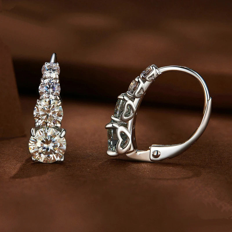 Une paire de boucles d'oreilles à clous en argent sterling 925 et moissanite, présentées sur une surface marron foncé.