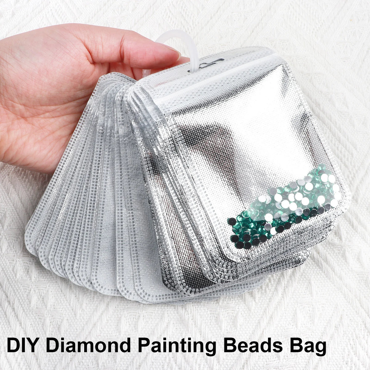 A hand holds a clear plastic bag filled with diamond painting beads for storage.