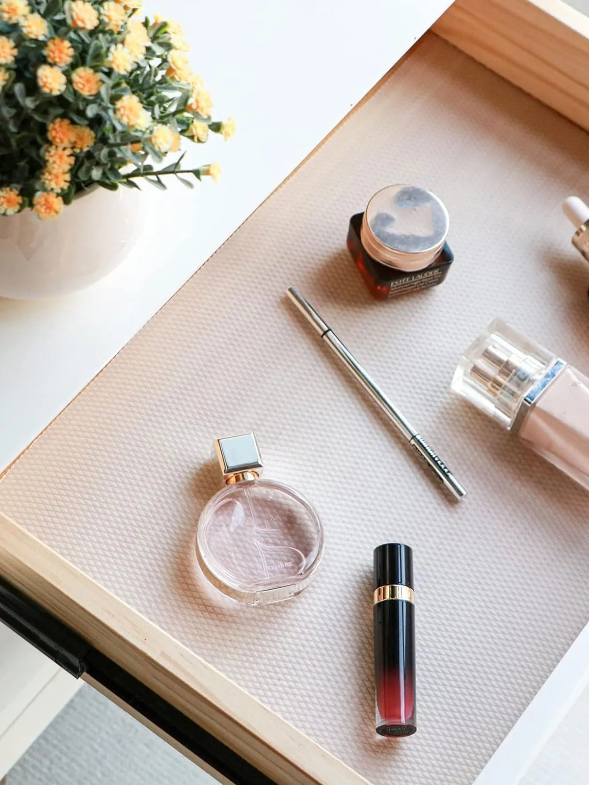 A close-up of a cosmetic product and various small items resting on a light beige drawer liner mat.