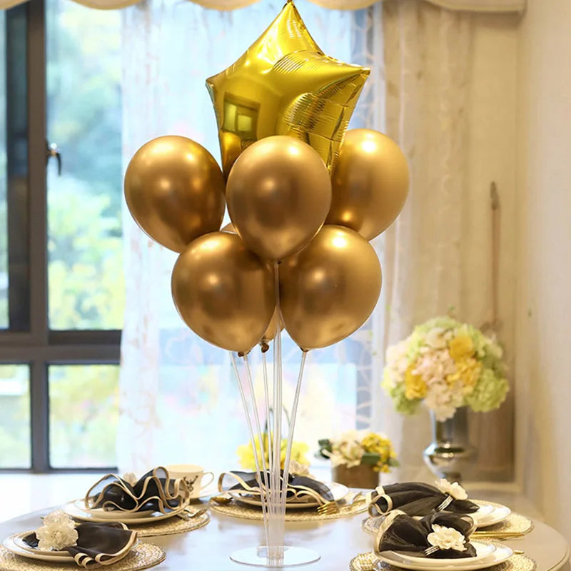 A column of gold and bronze balloons stands on a table with plates and floral arrangements.