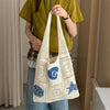A person holds a white handwoven knit tote bag with blue decorative stitching against a light background.