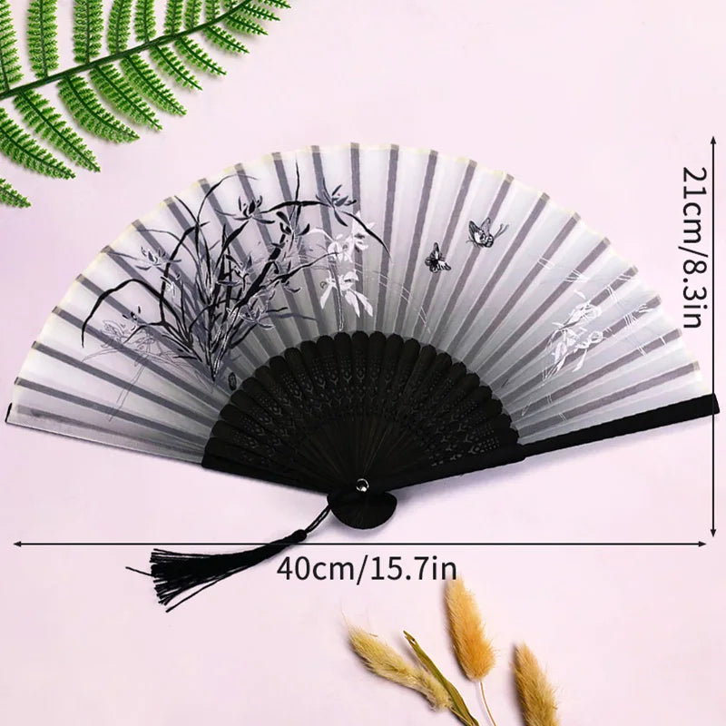 A black and white vintage lace folding hand fan with a durable handle displayed against a light pink background.