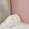 A fluffy white beaded chain shoulder clutch bag resting on a pink wall.