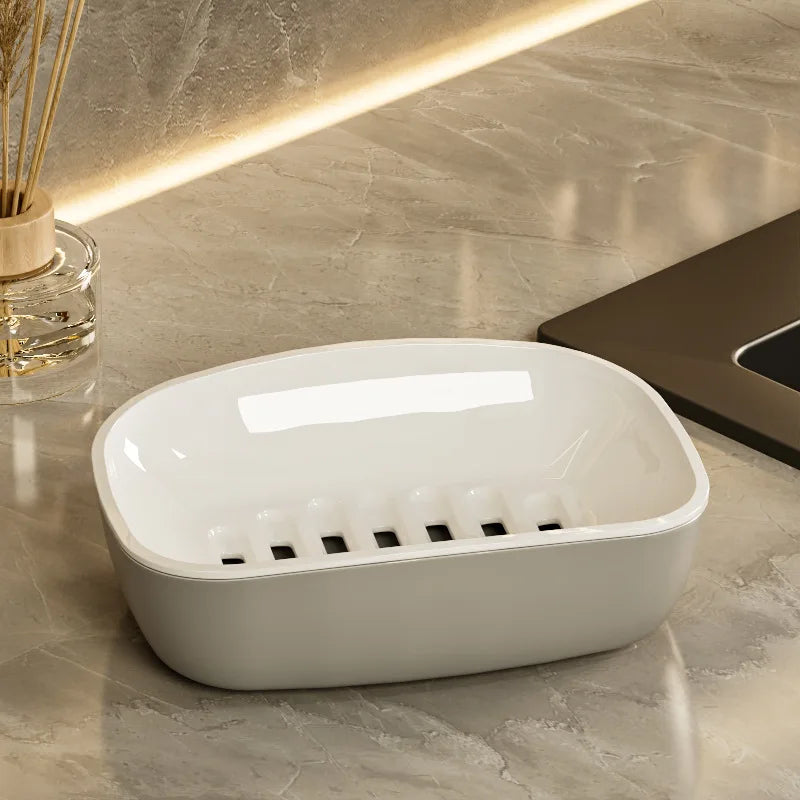 A white double-layer draining soap dish with a non-slip base resting on a marble surface.