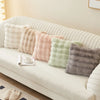 A collection of soft plush decorative pillows in pastel shades rests on a white sofa.