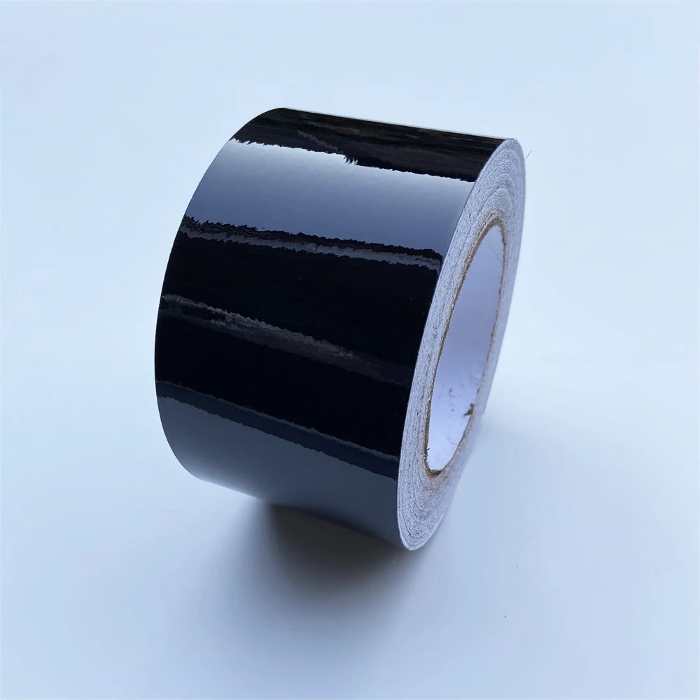 A roll of glossy black vinyl wrap strip for car trim and protection.