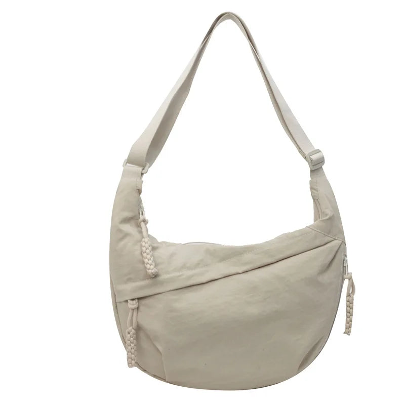 A light beige nylon crossbody bag with an adjustable strap shown from the front.