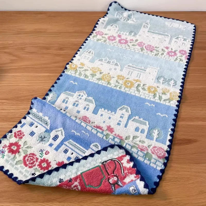 A rectangular blue and white embroidered cartoon face towel featuring various architectural scenes and floral patterns.