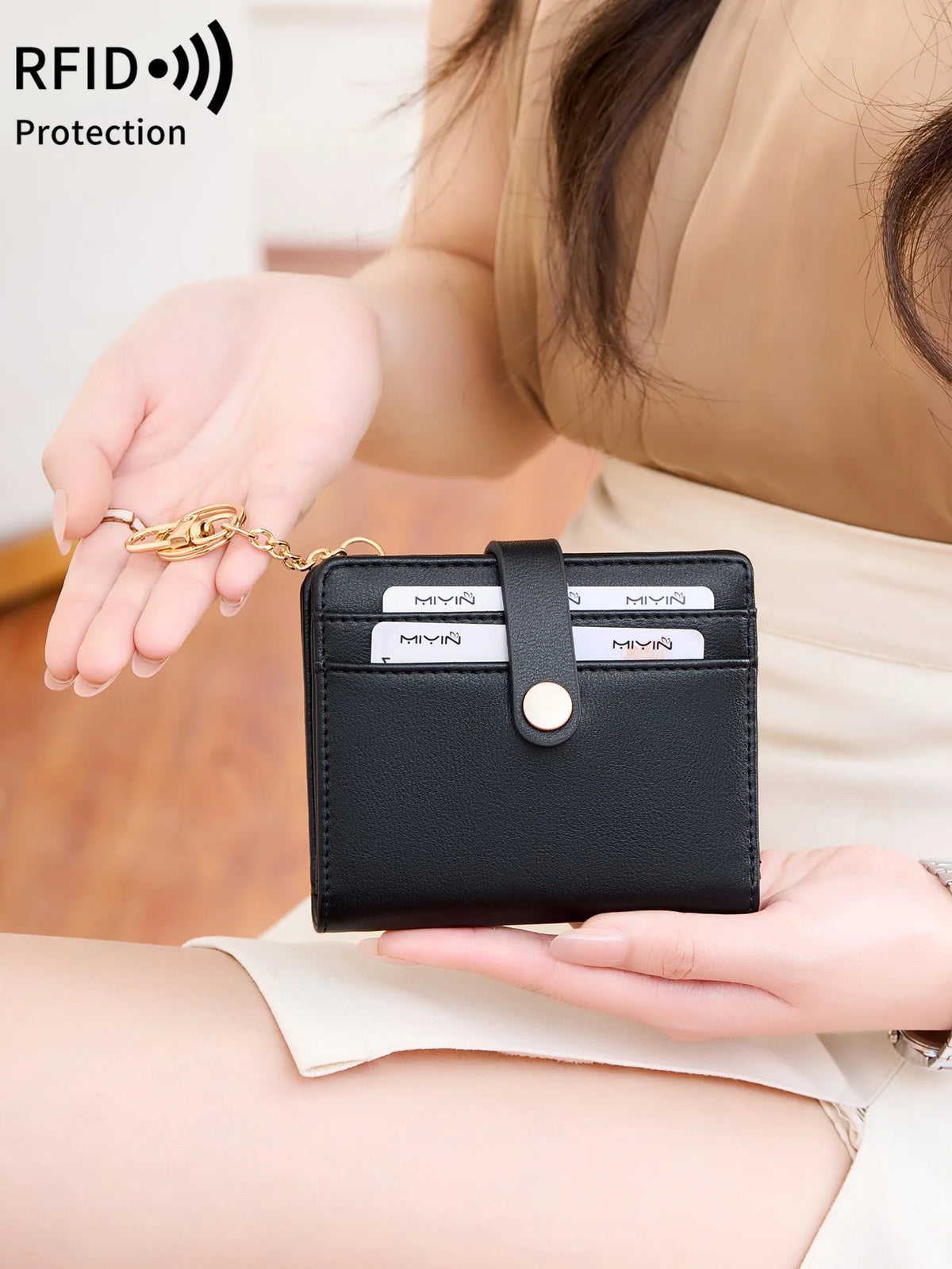 A hand holds a black bi-fold credit card wallet with a gold chain, demonstrating RFID protection.