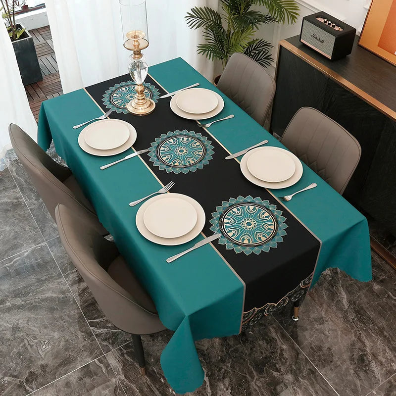 A long dining table set with a teal tablecloth, black and green placemats featuring geometric patterns, and gray chairs.