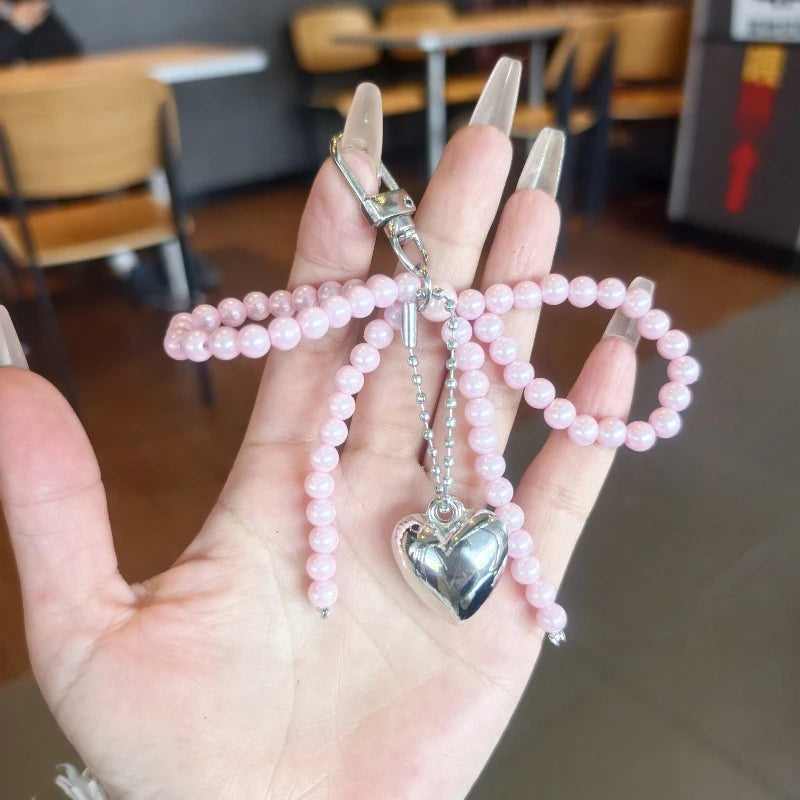 A hand holds a pearl bow keychain with a heart charm