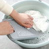 A hand places a non-slip laundry scrubbing board into a basin of soapy water.