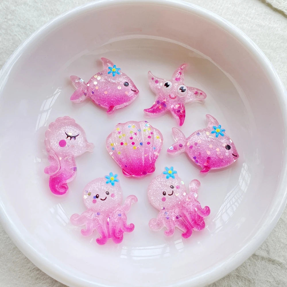 Pink glittery resin charms shaped like sea creatures and starfish arranged in a white bowl