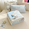 A set of light blue and white bedding featuring cute bear patterns and a stuffed teddy bear.