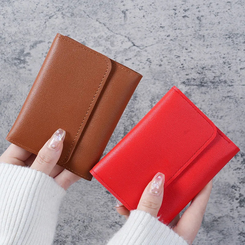 A hand holds a slim triple-fold PU leather wallet in shades of brown and red against a gray background.