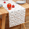 White table runner with black ghost pattern featuring autumn pumpkins on a wooden dining table.