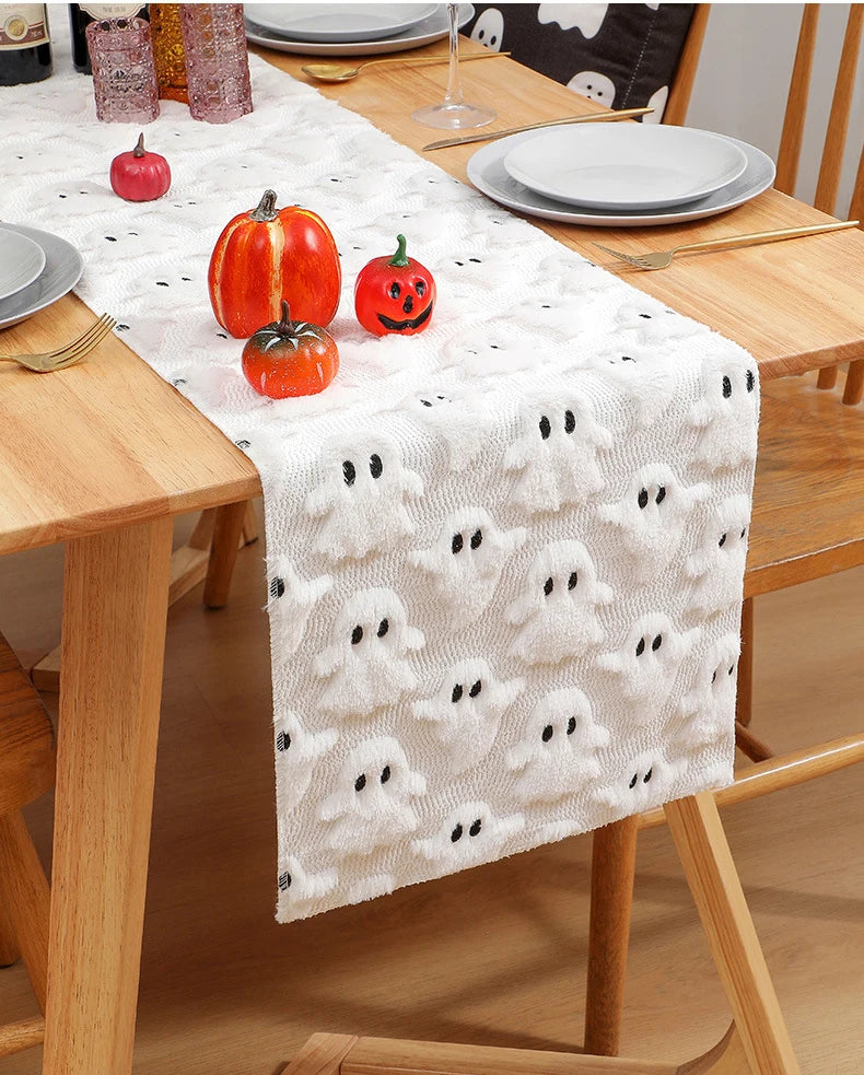 White table runner with black ghost pattern featuring autumn pumpkins on a wooden dining table.