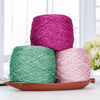Three skeins of metallic silk crochet yarn in shades of magenta, teal, and pink resting on a wooden tray.